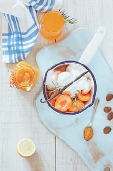 High angle view of sugared apricots in a pan, preserving jar and apricot juice, rustic style, on a wooden surface. Natural light