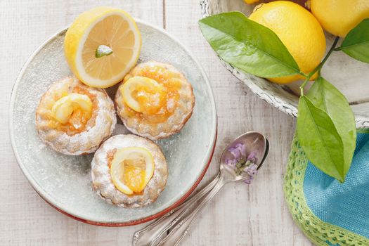 Mini lemon bundt cakes dusted with icing sugar and fresh lemons over rustic wooden background. Macro, selective focus. Natural light