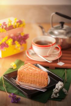 A piece of Thai tea cake on black ceramic dish with a cup of hot tea in background with morning scene