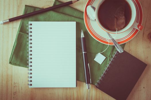 Opened notepad with pen and a cup of hot tea on wood table in cafe with film filter effect