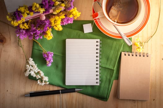 Opened notepad with pen and a cup of hot tea on wood table in cafe with morning scene