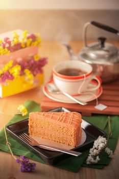 A piece of Thai tea cake on black ceramic dish with a cup of hot tea in background with morning scene