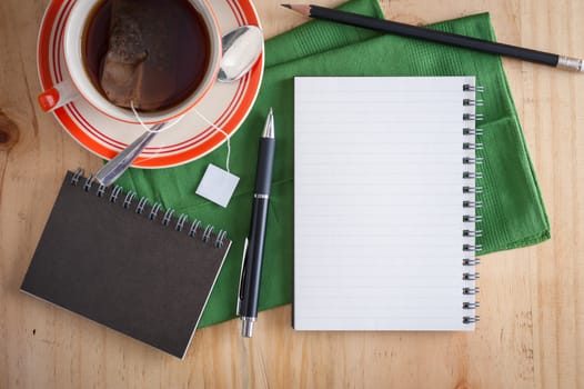 Opened notepad with pen and a cup of hot tea on wood table in cafe with morning scene