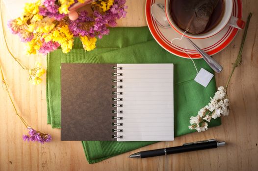 Opened notepad with pen and a cup of hot tea on wood table in cafe with morning scene