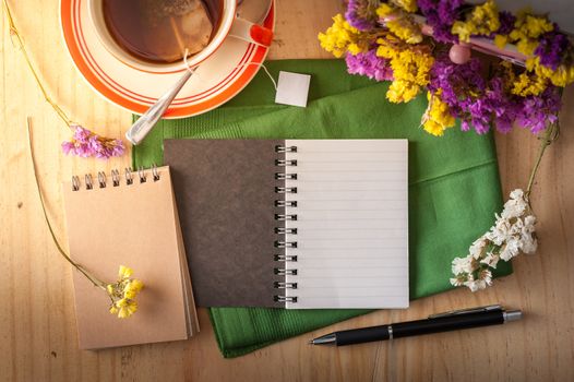 Opened notepad with pen and a cup of hot tea on wood table in cafe with morning scene