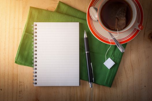 Opened notepad with pen and a cup of hot tea on wood table in cafe with morning scene