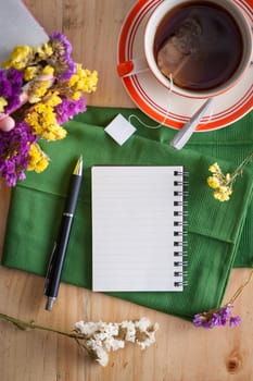 Opened notepad with pen and a cup of hot tea on wood table in cafe with morning scene