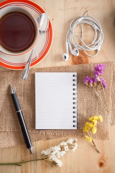 Opened notepad with pen, small earphone, and a cup of hot tea on wood table in cafe with morning scene