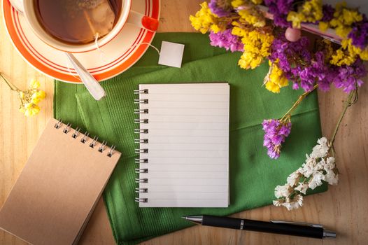 Opened notepad with pen and a cup of hot tea on wood table in cafe with morning scene