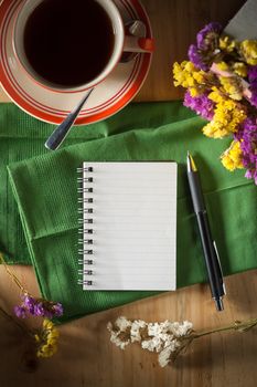 Opened notepad with pen and a cup of hot coffee on wood table in cafe with low key scene