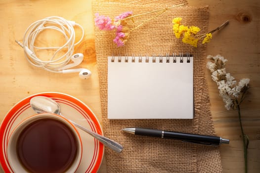 Opened notepad with pen, small earphone, and a cup of hot tea on wood table in cafe with morning scene