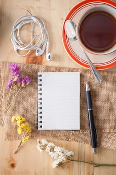 Opened notepad with pen, small earphone, and a cup of hot tea on wood table in cafe with morning scene