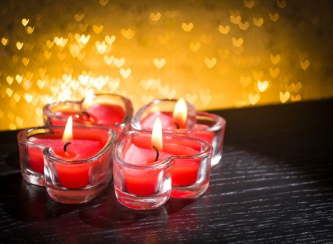 red burning heart shaped candles on golden hearts bokeh background