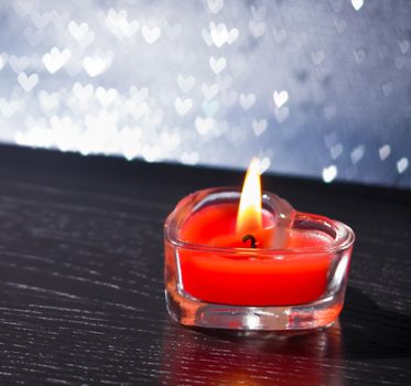 red burning heart shaped candle on silver hearts bokeh background, valentine day and love concept