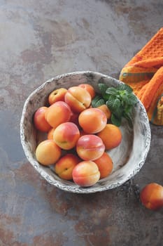 Bowl of harvested apricots on a rustic stone surface, top view, rustic style. Natural light