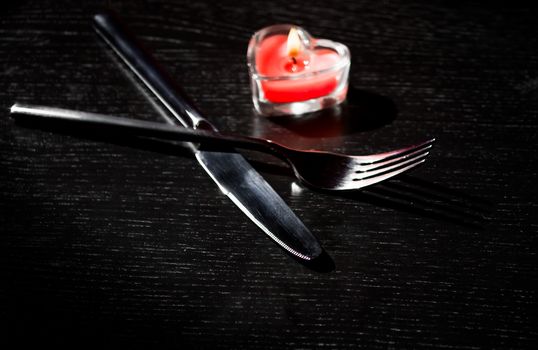 Valentine day table setting with knife, fork, red burning heart shaped candle, holiday and Valentines day background