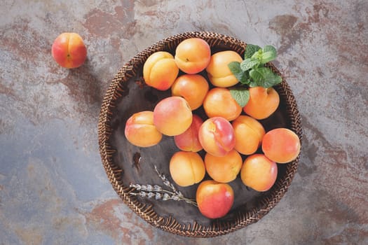 Fresh apricots in wooden bowl on old rustic background decorated with mint and lavender flower. Top view, rustic style. Natural light