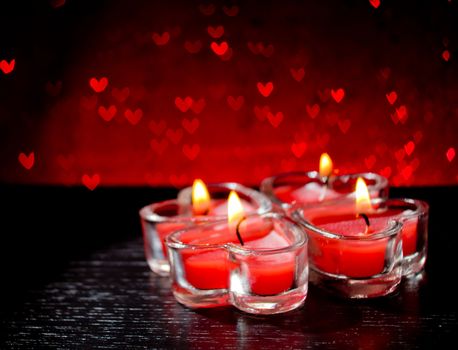 red burning heart shaped candles on red hearts bokeh background