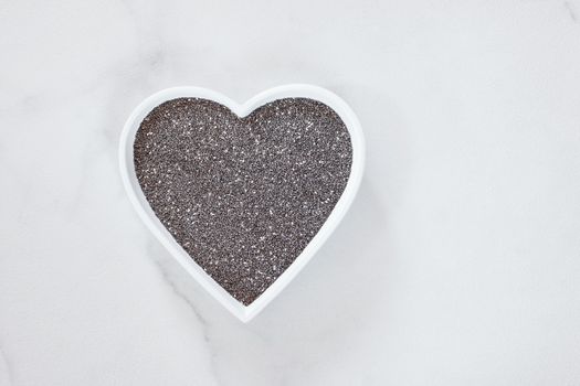 Raw whole chia seeds in a hearts shaped dish. Natural light