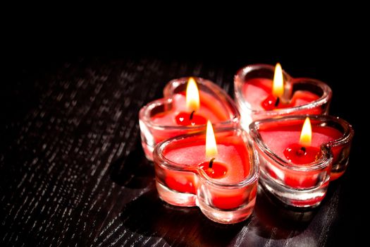 red burning heart shaped candles on black wood table, valentine day and love concept