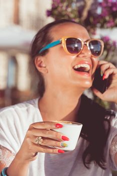 Smiling woman drinking coffee in cafe and talking on cell phone. Focus on cup of coffee