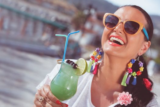 Happy young woman holding a glass of cocktail near the yacht marine.