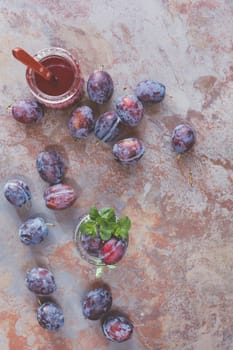 Fresh scattered plums and plum juice in jar on rustic background. Vintage style, top view