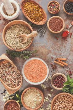 Various types of grains, rice, legumes spices and herbs in bowls on rustic table, top view