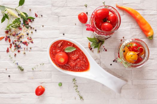 Spicy tomato jam on spoon and fresh tomatoes in a glass jar, top view