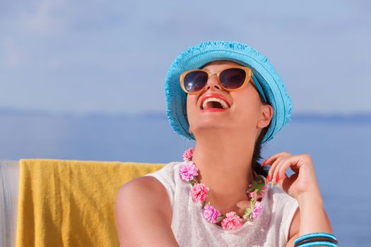Happy woman with straw hat sitting on lounge chair at the beach and enjoying her beach vacation