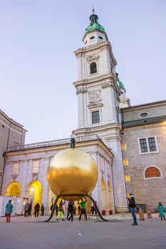 Salzburg, Austria - December 31, 2013: Golden sphere with man standing on it at Kapitelplatz at night - Cathedral of Salzburg in the background.