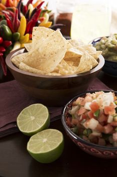 Fresh tortilla chips with pico de gallo and fresh limes in forground, guacamole and a margaritia in the background.
