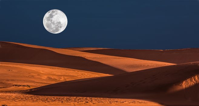 Large full moon rising over orange sand dunes