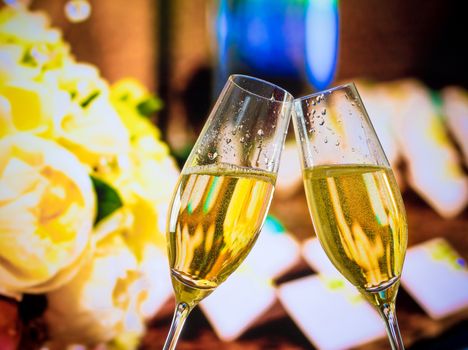 champagne flutes with golden bubbles make cheers on wedding flowers background