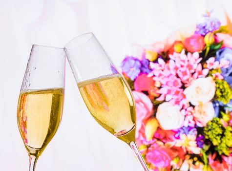 champagne flutes with golden bubbles make cheers on wedding flowers background