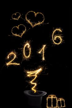 Magical new year. Magical fireworks from black top hat forming the digits 2016, gifts and heart shape isolated on black background. Happy new year background.