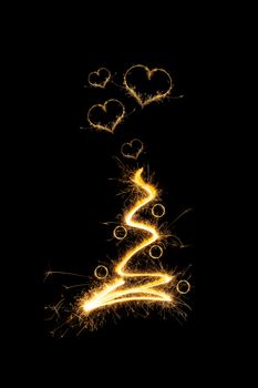 Abstract lightning sparkling christmas tree with christmas balls and heart shaped sparkles isolated on black background. Magical christmas.