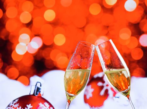 champagne flutes with golden bubbles make cheers on red christmas lights bokeh and balls decoration background, christmas atmosphere