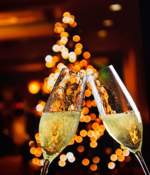 champagne flutes with golden bubbles make cheers on christmas lights decoration background, christmas atmosphere