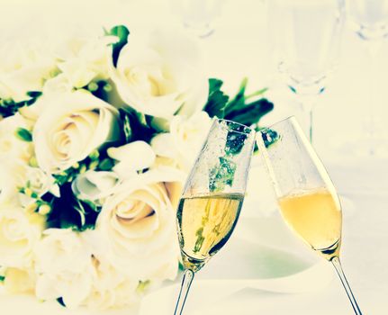 champagne flutes with golden bubbles make cheers on wedding flowers background, vintage style