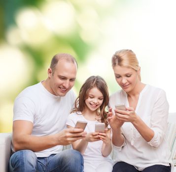 family, summer, technology and people concept - smiling mother, father and little girl with smartphones over green background