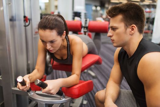 sport, fitness, lifestyle and people concept - young woman and personal trainer flexing leg muscles on gym machine