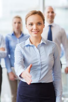 business, people and teamwork concept - smiling businesswoman making handshake gesture with group of businesspeople in office