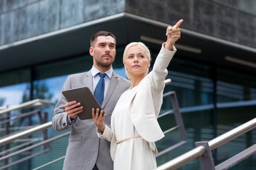 business, partnership, technology and people concept - serious businessman and businesswoman with tablet pc computer over office building