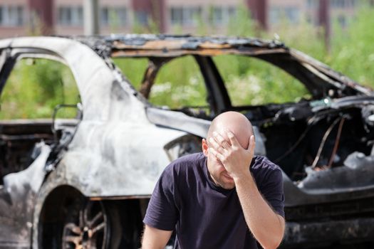 Crying upset caucasian man at road wreck accident or arson fire burnt wheel car vehicle junk