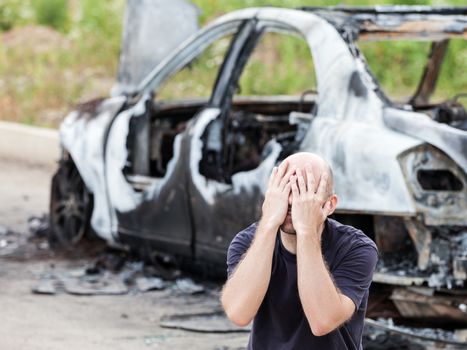 Crying upset caucasian man at road wreck accident or arson fire burnt wheel car vehicle junk