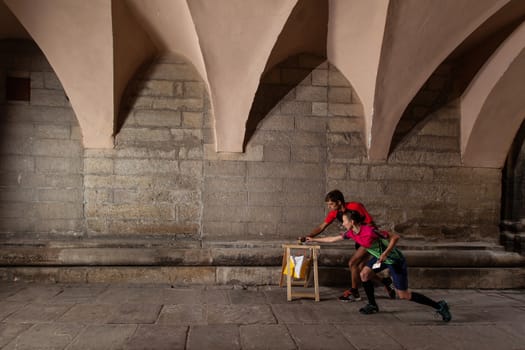 Two sportsmens punching at control point, taking part in orienteering city race competitions in old european city