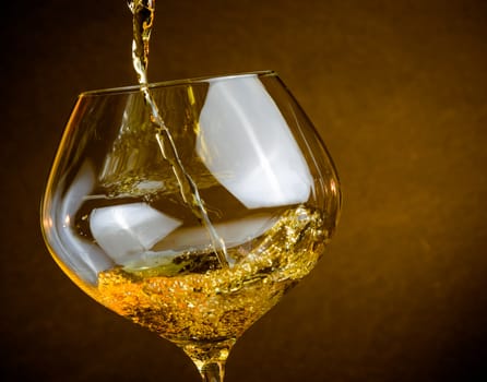 pouring white wine into a glass on golden background with space for text, warm atmosphere