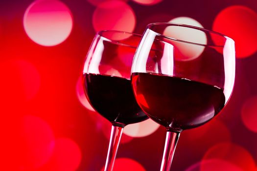 two red wine glasses against red bokeh lights background, festive and fun concept