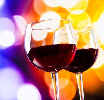 two red wine glasses against colorful bokeh lights background, festive and fun concept